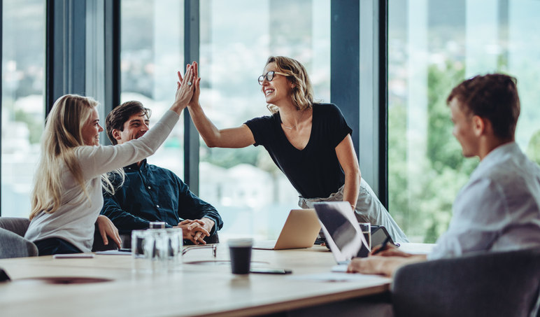 two-people-reaching-over-and-high-fiving-each-other-while-sitting-at-a-table