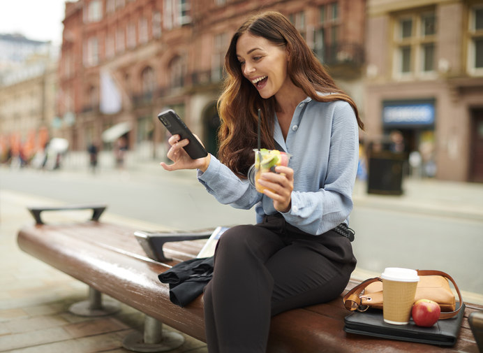 a-woman-sitting-on-a-bench-while-drinking-a-drink-and-looking-at-her-phone