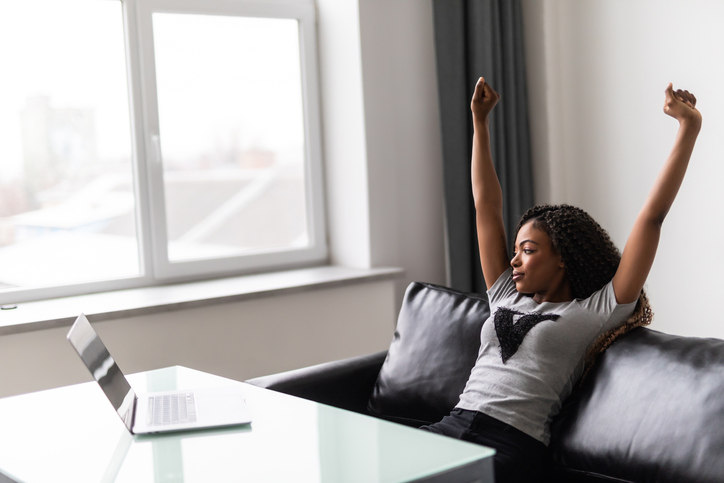 woman-sitting-on-couch-stretching-with-computer-on-table-in-front-of-her