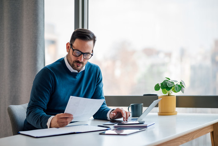 a-man-sitting-at-a-desk-inputting-information-from-a-piece-of-paper-into-a-computer