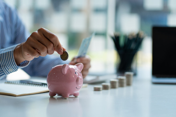 person-dropping-coin-into-piggy-bank-while-counting-money