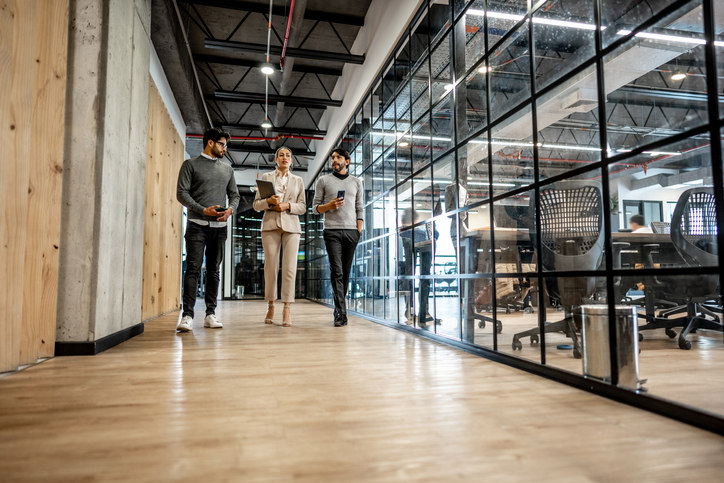 three-people-walk-down-a-hallway-in-an-office-and-chat