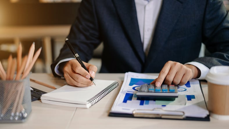 person-sitting-at-a-desk-writing-down-numbers-from-a-calculator