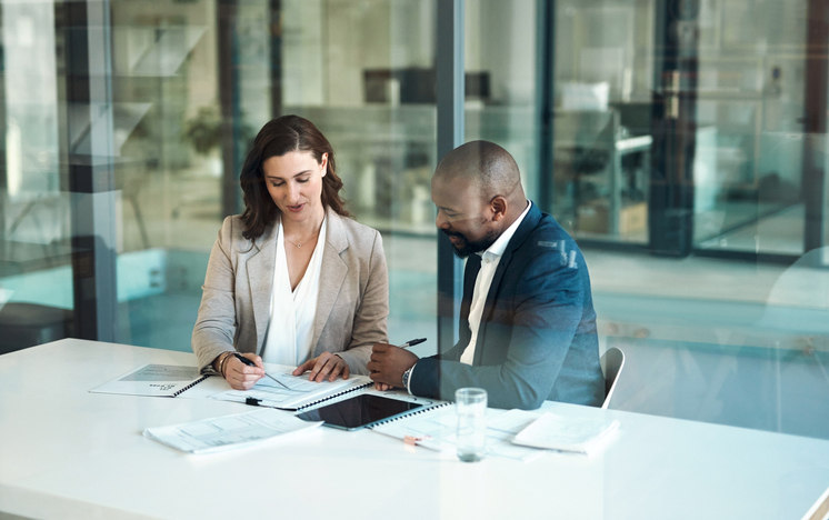 two-people-sitting-at-a-table-in-a-conference-room-looking-over-documents