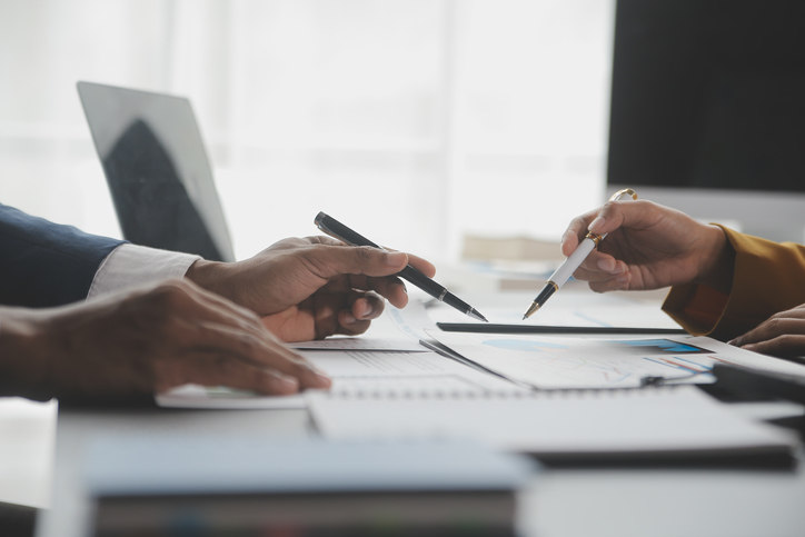 people-looking-over-papers-on-a-desk-with-pens-in-their-hands