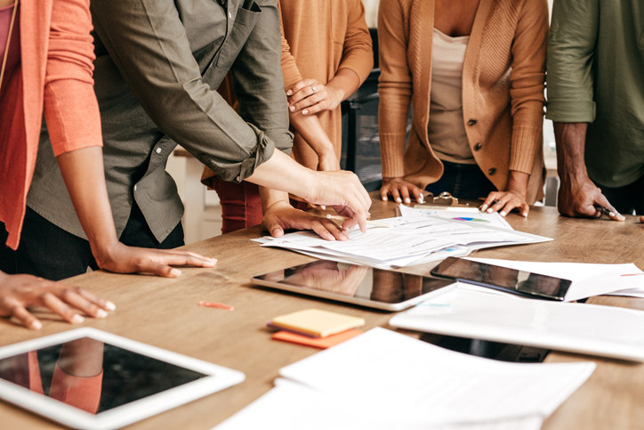 a-group-of-people-stand-around-a-table-looking-at-papers