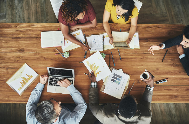 a-group-of-people-sitting-at-a-table-looking-over-various-data-sheets