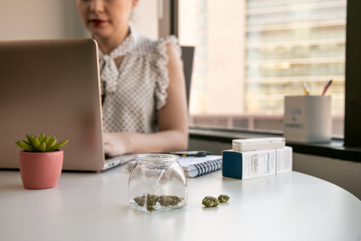 woman-sitting-at-a-desk-working-on-a-computer-with-a-jar-of-marijuana-nugs-sitting-on-the-desk