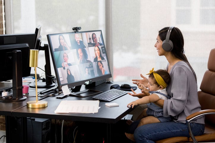 a-woman-sits-at-a-desk-during-a-video-conference-with-a-child-in-her-lap