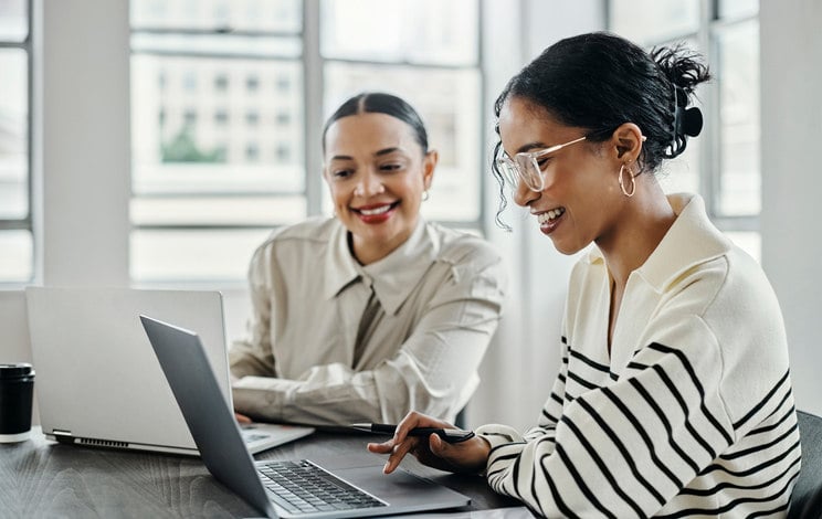 two-people-sitting-together-at-a-desk-looking-at-a-laptop