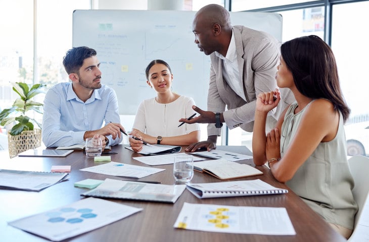 a-man-talks-to-a-group-of-people-sat-around-a-table