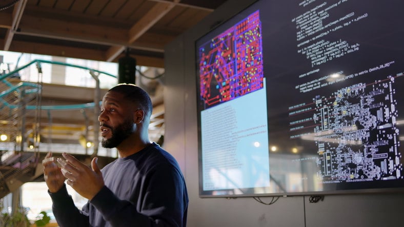 a-man-stands-in-front-of-a-group-of-tvs-and-gives-a-presentation